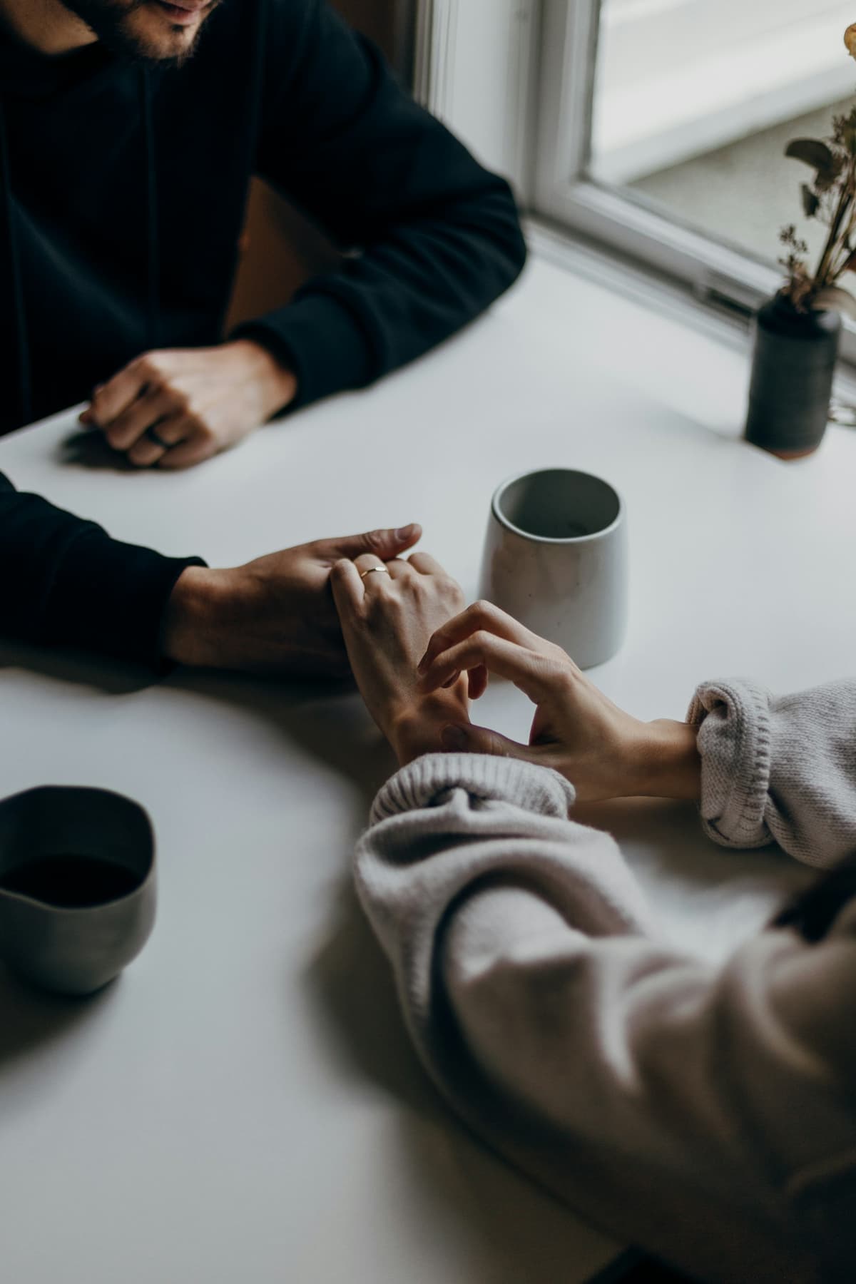Zwei Menschen sitzen sich am Tisch gegenüber, Kaffeetassen und Hände