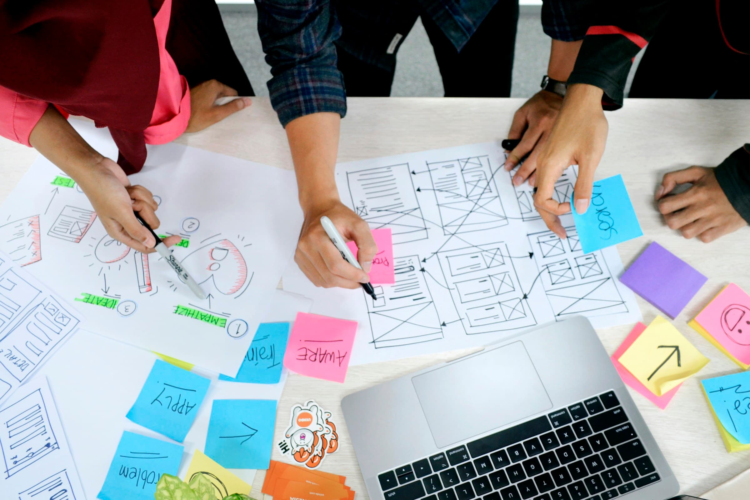 Hände über einem Tisch mit Skizzen, Post-its und Laptop im Workshop