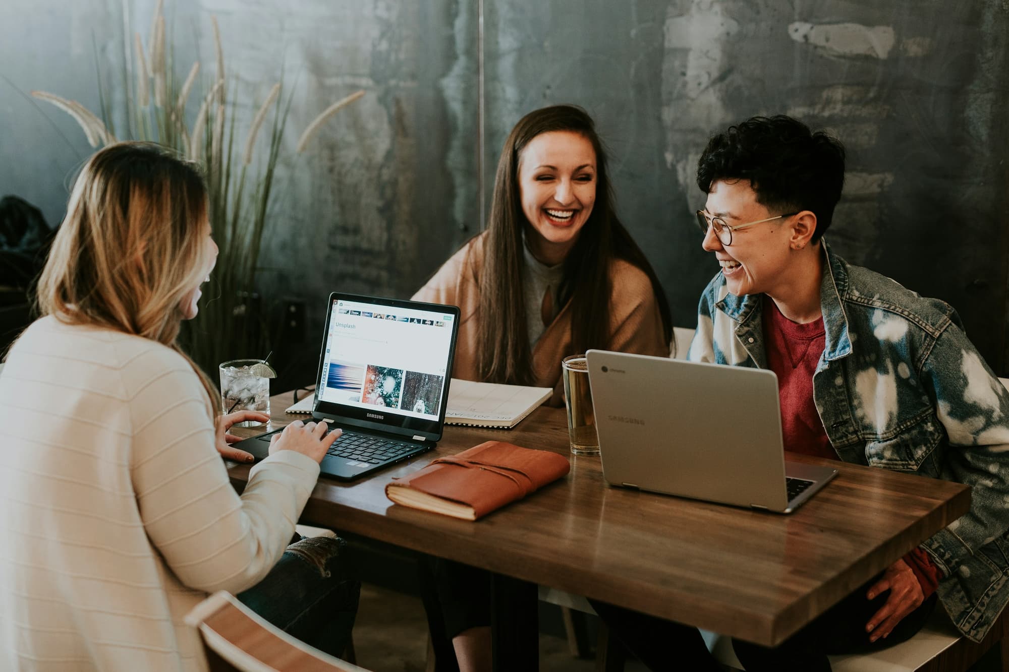 Drei Menschen lachen gemeinsam am Tisch mit Laptops